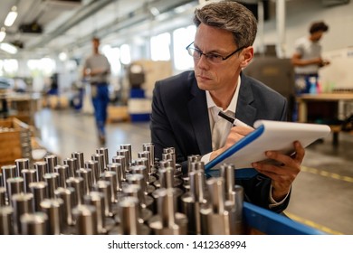 Quality control inspector writing reports while analzying manufactured steel rod cylinders in industrial building.  - Powered by Shutterstock