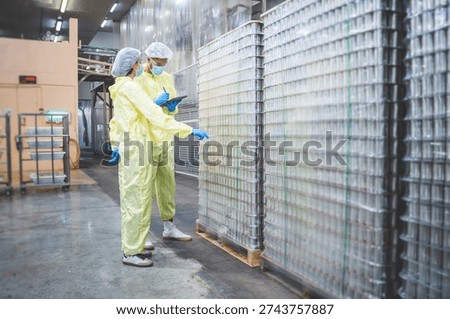 Quality control inspectors using tablet to check stock of empty cans in a large food factory warehouse, Factory workers performing a digital inventory audit in a clean industrial manufacturing plant