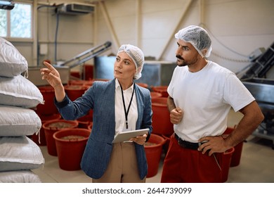 Quality control manager talking to a worker while inspecting processed goods in food factory. 