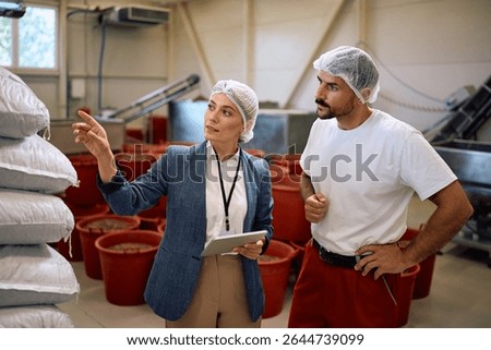 Quality control manager talking to a worker while inspecting processed goods in food factory. 