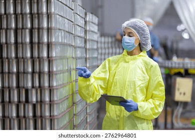 Quality control worker inspecting stacked canned fish products in seafood factory warehouse. Industrial food processing, packaging plant maintaining hygiene standards, export manufacturing compliance.