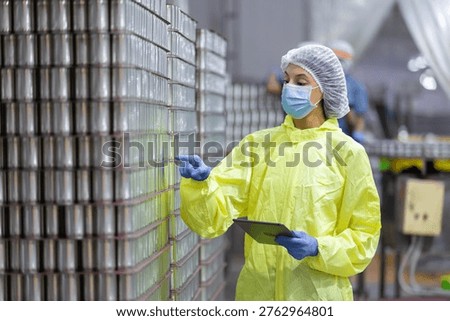 Quality control worker inspecting stacked canned fish products in seafood factory warehouse. Industrial food processing, packaging plant maintaining hygiene standards, export manufacturing compliance.