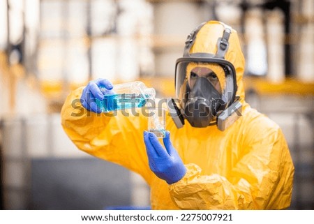 Quality control worker in protection suit and gas mask testing quality of chemical inside chemicals production factory .
