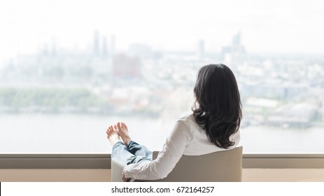 Quality Of Life Concept Of Business Woman Rear View Relaxing Sitting In Rest On Armchair In Modern Hotel Guest Room Or Luxury Home Living Room Looking Outward To City Urban Scene