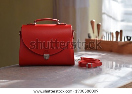 Quality luxury handmade women's bag. Women's leather handbag with a strap next to it. Red modern women's bag. A photo taken in a bag workshop. 