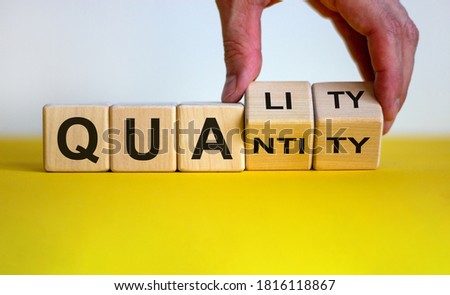 Quality over quantity. Hand turns cubes and changes the word 'quantity' to 'quality'. Beautiful yellow table, white background, copy space. Business concept.