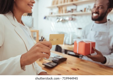 Quality service. The focus being on the hands of a beautiful young woman holding a golden card and being ready to pay for her order in the coffeehouse