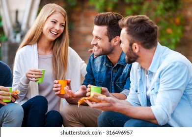 Quality Time With Best Friends. Group Of Happy Young People Talking To Each Other And Eating Pizza While Sitting Outdoors