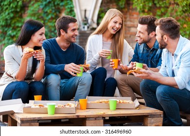 Quality Time With Friends. Group Of Joyful Young People Talking To Each Other And Eating Pizza While Sitting Outdoors