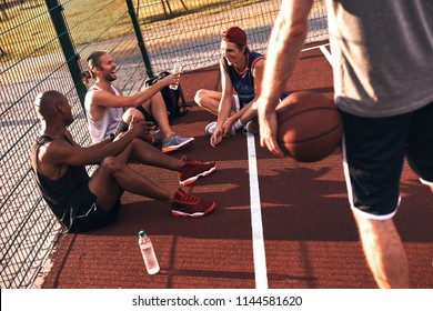 Quality Time With Friends. Top View Of Young Men In Sports Clothing Smiling While Sitting On The Basketball Field Outdoors    