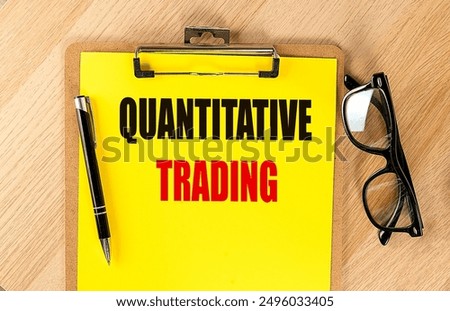 QUANTITATIVE TRADING text on yellow paper on a clipboard with pen and glasses. 