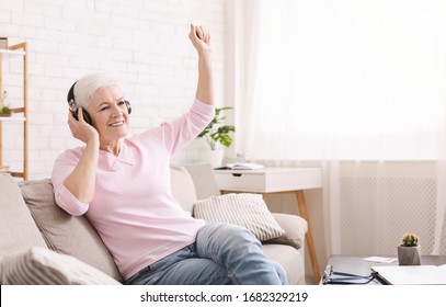 Quarantine can be fun. Joyful senior lady enjoying music in new headset at home, empty space