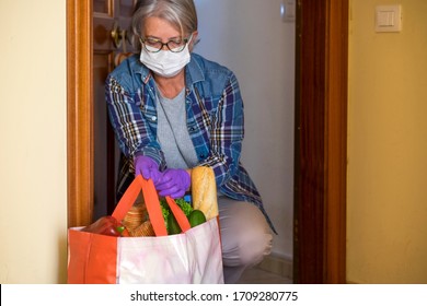 Quarantine For Coronavirus Covid-19 Pandemic. Casual Senior Woman With Protective Gloves Receives Grocery Delivery At Home With Basic Necessities. Concept Of Staying Home To Avoid Contagion