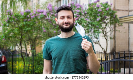 Quarantine is over concept.Smiling young brunette man taking off medical protective mask looking at camera,standing outdoor city.Happy male breathing deep fresh summer air.Freedom,end of coronavirus - Shutterstock ID 1775343293
