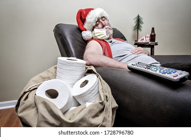 Quarantine Santa Claus Sleeping In An Recliner With Face Mask And Pack Full Of Toilet Paper, Focus On Chair Arm And Remote And Toilet Paper