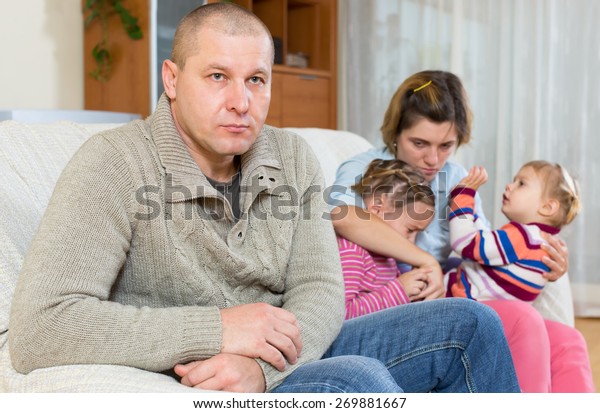 Quarell in\
a family. Sad husband on the front and his wife and two crying\
upset daughters in the back sitting on a\
sofa