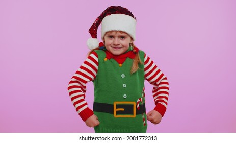 Quarrel. Displeased Baby Girl Kid In Christmas Santa Claus Helper Elf Costume Gesturing Hands With Irritation And Displeasure, Blaming Scolding For Failure, Asking Why This Happened. Happy New Year