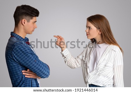 Quarrel, problems, negative emotions, freaking out and scandal. Angry nervous young lady points her finger at husband and accuses he, isolated on gray background, studio shot, side view, copy space