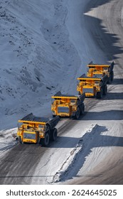 Quarry dump trucks queue for refueling in open pit coal mining, winter landscape.