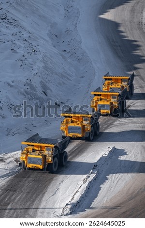 Quarry dump trucks queue for refueling in open pit coal mining, winter landscape.