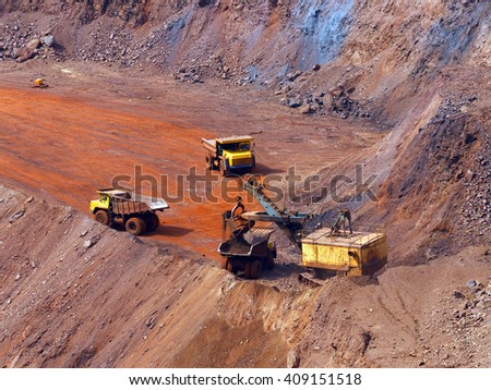 Quarry excavator load the iron ore to big dump truck in openpit mine with another two trucks waiting in queue