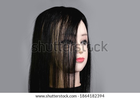 Quarter view of a mannequin head wearing a long black wig or toupee. Strands of hair partially cover right side of face.