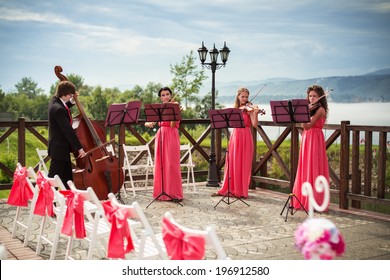 Quartet Of Classical Musicians Playing At A Wedding Outdoors Near The River