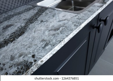 Quartz counter worktop with beautiful pattern and stainless steel sink on black wooden kitchen.