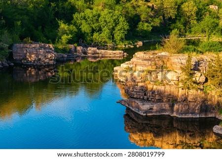 Quartzite rock cliffs and trees reflecting in calm waters of Split Rock Creek at Palisades State Park, South Dakota