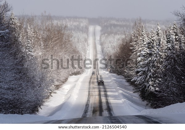 Quebec 216 road, in the region of\
Chaudière-Appalaches, in winter with a large panoramic view on the\
snowed forest bordering the partial snowed\
road.