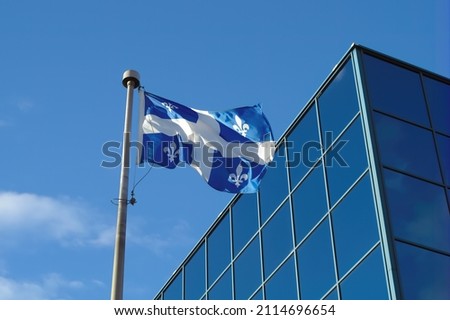 Quebec, Canada flag fluttering in the wind in front of a blue glass building sky and clouds canadian french culture symbol