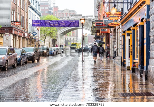 Quebec City, Canada - May 31, 2017: Old town\
street Saint-Jean during heavy rain with drops and wet road with\
couple walking