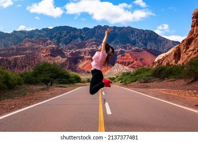 Quebrada de la Conchas, Salta Argentina. Woman jumping happily on the empty road. Woman on vacation in Argentina. Tourism in Argentina. Empty road surrounded by beautiful mountain landscape