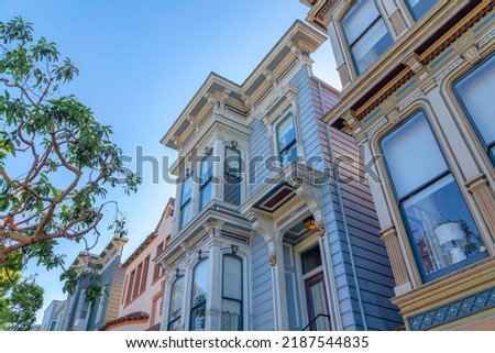 Queen anne row houses in a low angle view in San Francisco, California. Facade of houses with painted wood sidings and decorative colorful dentils and and bracket details.