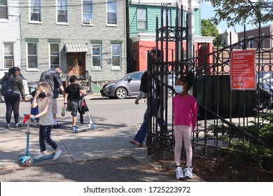 Queens, New York / United States - May 7 2020: Children Wearing Face Masks Outside Park Next To Playground Closed City Sign During Coronavirus Pandemic