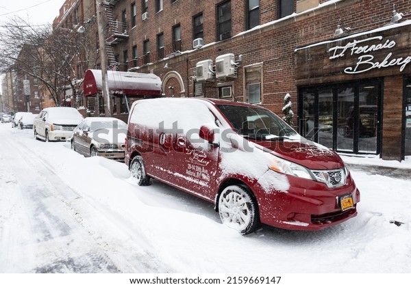 Queens, New York USA - January 29 2022: Parked\
Cars along a Snow Covered Street and Sidewalk in Astoria Queens New\
York during the Winter