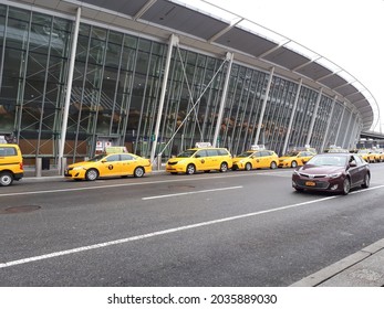 Queens, NY, USA - Feb 12, 2018: NYC Taxis parking next to the airport terminal at John F. Kennedy International Airport and a car driving by