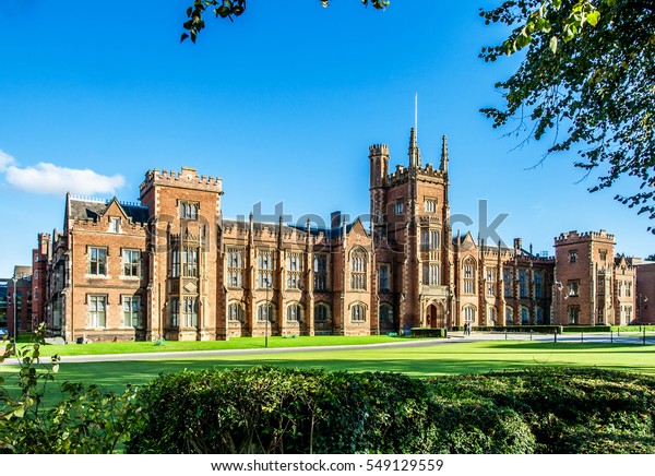 The Queen\'s University of Belfast\
with a grass lawn, tree branches and a hedge in sunset\
light