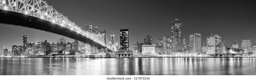 Queensboro Bridge over New York City East River black and white at night with river reflections and midtown Manhattan skyline illuminated.