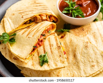 Quesadillas with tomato sauce. Traditional mexican food. Grilled corn tortillas wraps with chicken fillet, vegetables and parsley. Tasty snack. Closeup view.
