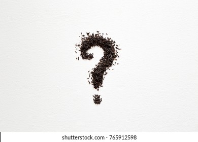 Question mark created from black, dried, loose tea on the white table. Choice of the best sort and quality tea. Empty place for a text.