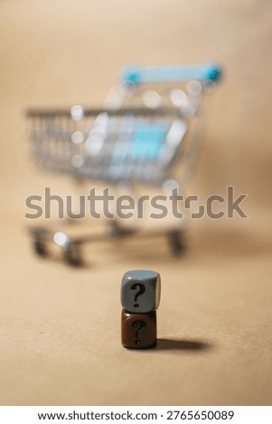 Question mark cube in focus with blurred shopping cart on beige background. Uncertainty and purchase decision concept.