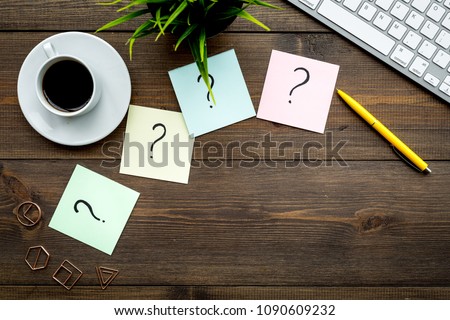 Question mark on sticky notes on office desk on dark wooden background top view copy space. FAQ concept. Working with clients. Troubles in work.