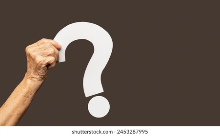 Question mark symbol. Hand holding a white question mark symbol against a brown background. Close-up photo. Space for text - Powered by Shutterstock