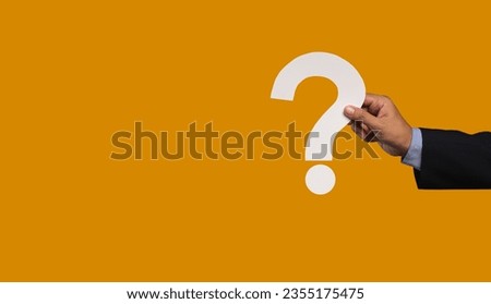 Question mark symbol. Hand holding a white question mark symbol against an orange background. Close-up photo. Space for text