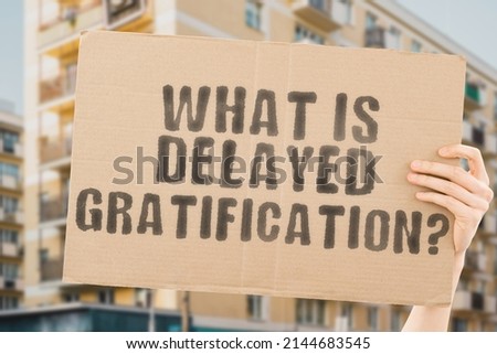 The question " What is delayed gratification? " on a banner in men's hands with blurred background. Happy. Delay. Business. Pause. Later. Await