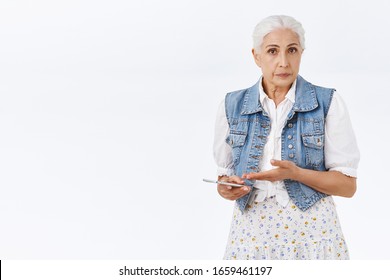 Questioned And Upset Old Woman, Senior Lady Cant Understand How Log In To Mail Using Smartphone, Hold Mobile Phone, Pointing Confused At Device And Look Camera, Puzzled And Indecisive