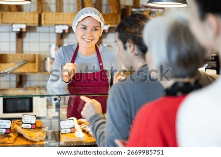 Queue of customers is lined up at counter of bakery. People place order at bakery, buy sweet pastries in cafeteria, girl worker serving people