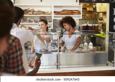 A Queue Of Customers Served By Two Women At A Sandwich Bar