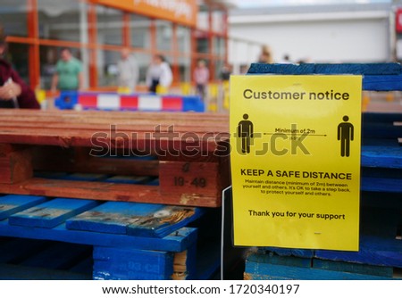 Queue of people waiting to get into a hardware store in the Uk during the coronavirus pandemic with sign in the foreground telling people to stay two metres apart